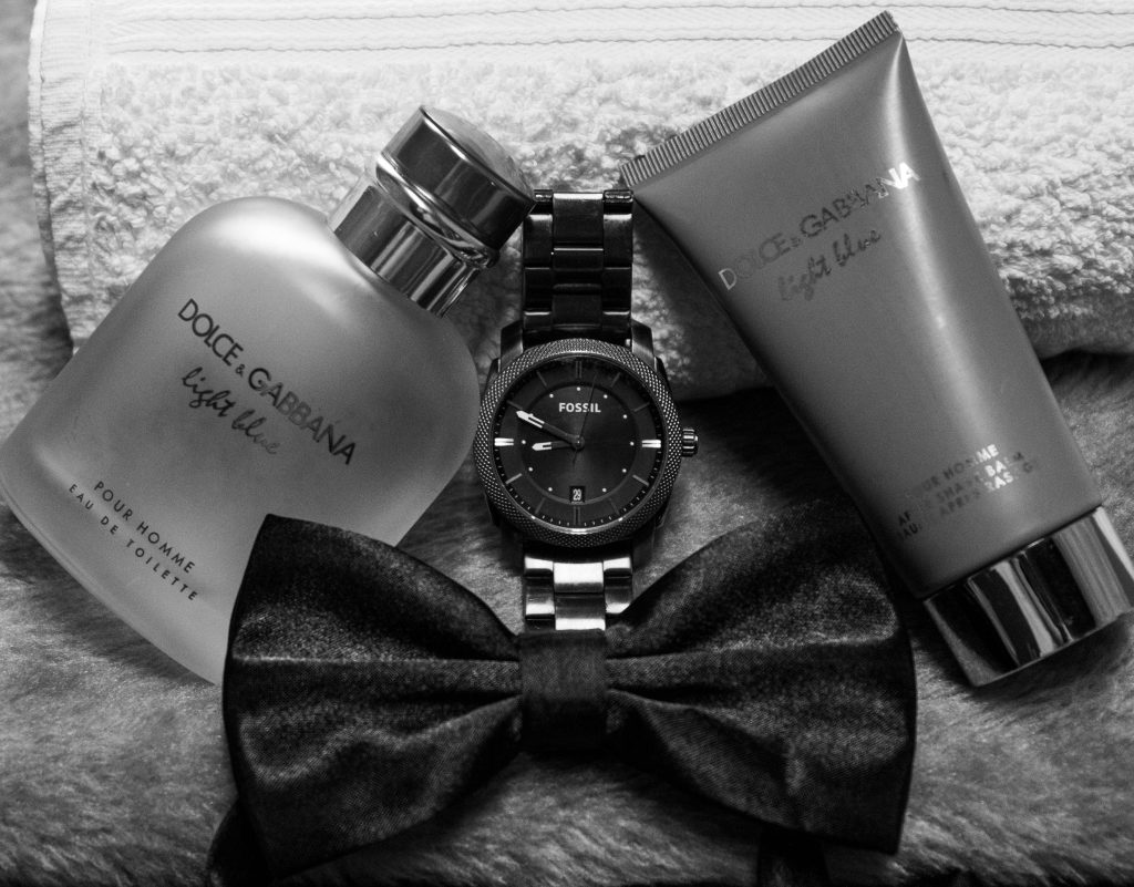 Black and white still life featuring a watch, bow tie, and Dolce & Gabbana perfume for men.